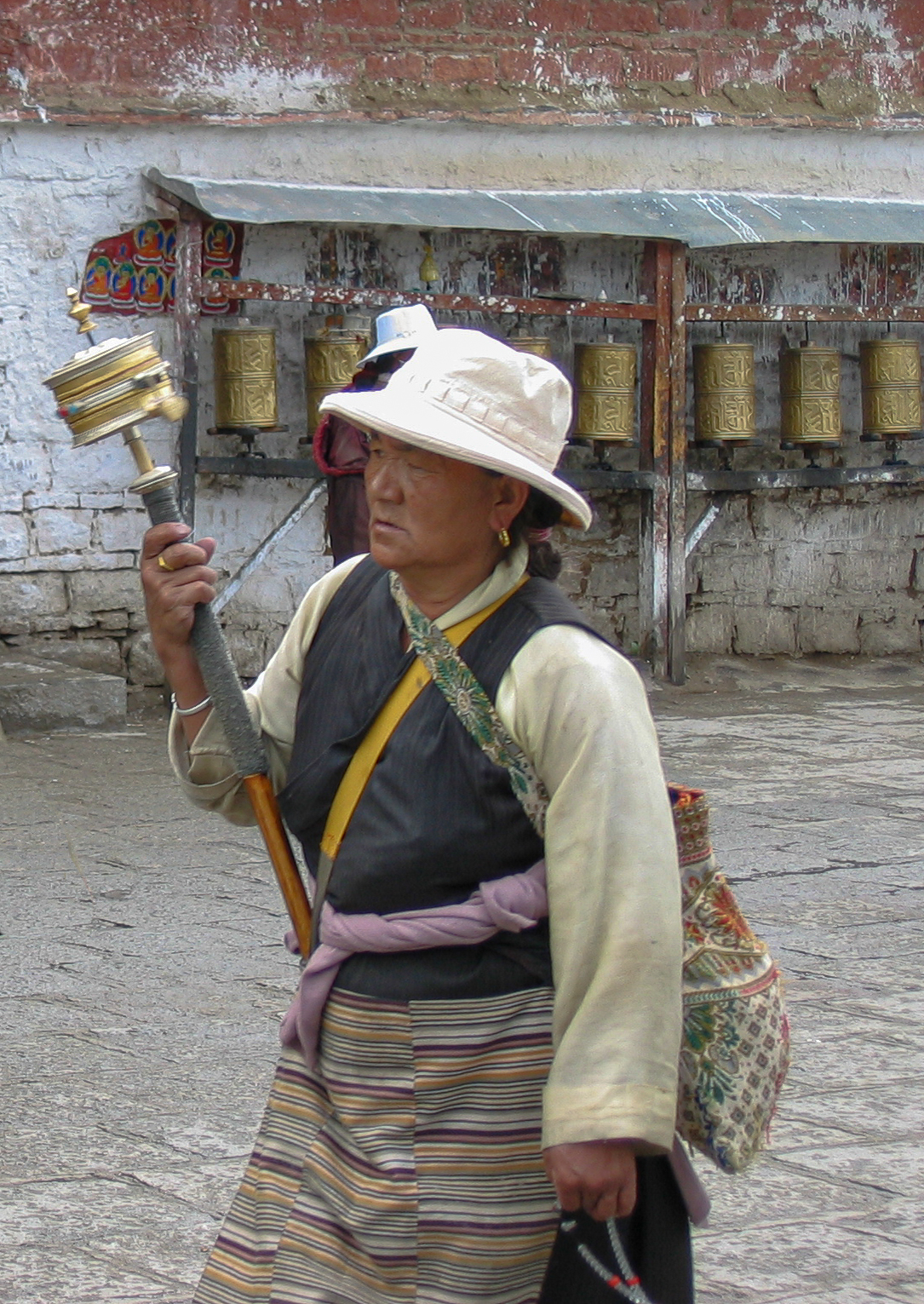 A Tibetan woman whirling her prayer wheel - in the background larger prayer wheels ready for follows to turn. The Barkhour. Lhasa.